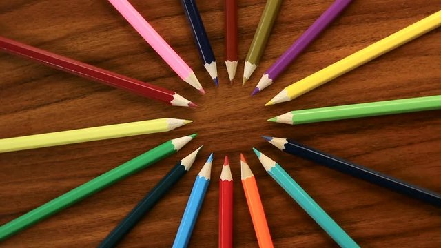 A lot of multicolored pencils revolve in a circle on a black wooden background. Concept office or school, knowledge day, the first of September. Video footage is spinning