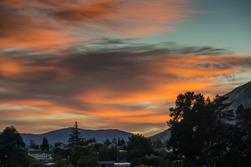Queenstown, New Zealand - March 16, 2017: Sunrise over the town paints parts of sky orange, offset by dark clouds, as if the horizon is on fire. Greenish sky breaks from the right which is the north.
