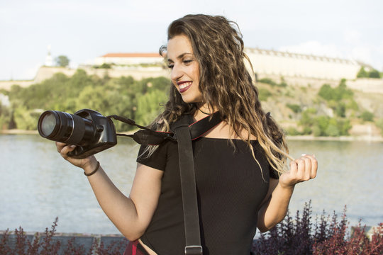 Woman tourist on the street. Under sunlight and blue sky. Female photographer with a professional camera. Portrait of a beautiful laughing brunette girl, making photos by the river.