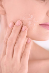 Beautiful young woman applying cream onto face