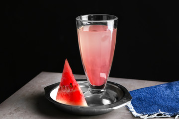 Plate with refreshing drink in glass and watermelon slice on table