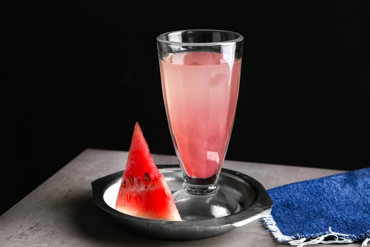 Plate with refreshing drink in glass and watermelon slice on table