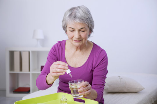 Senior Woman Pouring Essential Oil In A Glass Of Water