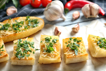 Tasty bread slices with grated cheese, garlic and herbs on parchment