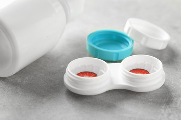 Container with contact lenses and bottle of solution on gray table