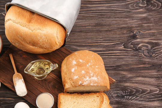 Loaf In Bread Machine Pan And Ingredients On Wooden Table