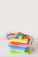 Colored fabric folded stack. Needle bed, scissors, measuring tape. Beige background.