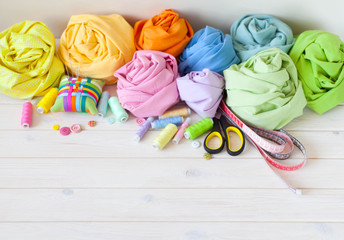 Colored fabric folded stack. Needle bed, scissors, measuring tape. Beige background.