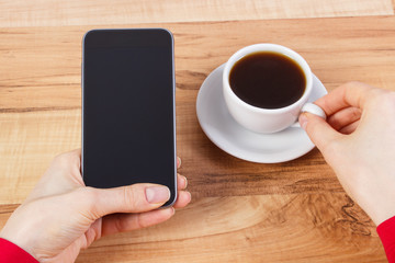 Hand of woman touching screen of mobile phone or smartphone, cup of coffee