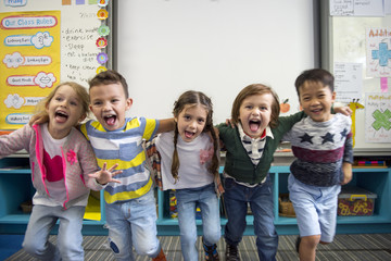 Group of diverse kindergarten students standing together in classroom - obrazy, fototapety, plakaty