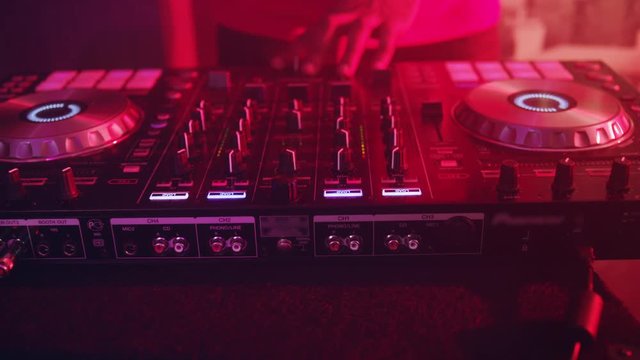 DJ control music console in nightclub. DJ mixer player. Close up DJ control sound console of disco. Disc jockey turntables and mixing deck with colored illuminated. DJ hands mixing music