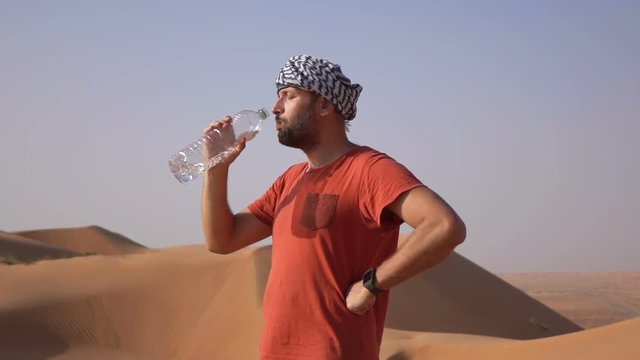 Young man drinking water standing on desert, super slow motion 240fps
