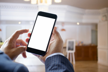  Traveler using smartphone at check-in information in front of the hotel reception desk. Blank screen smart phone for graphic display montage.