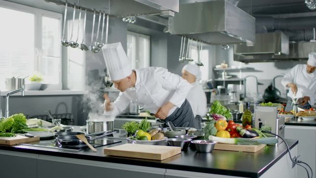 Famous Chef Works in a Big Restaurant Kitchen with His Apprentices. Kitchen is Full of Food, Vegetables and Boiling Dishes. Shot on RED EPIC-W 8K Helium Cinema Camera.