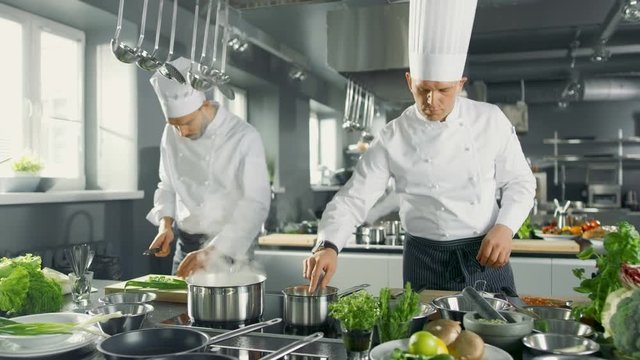 Two Famous Chefs Work as a Team in a Big Restaurant Kitchen. Vegetables and Ingredients are Everywhere, Kitchen Looks Modern with Lots of Stainless Steel. Shot on RED EPIC-W 8K Helium Cinema Camera.