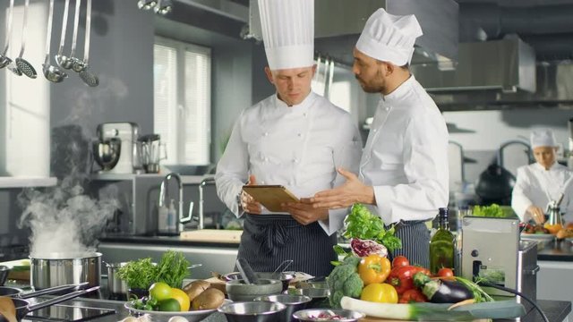 Two Famous Chefs Discuss Their Video Blog while Using Tablet Computer. They Work in Big Restaurant Stainless Steel Professional Kitchen. Shot on RED EPIC-W 8K Helium Cinema Camera.