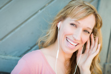 Fototapeta premium Outdoor Portrait of Young Adult Brown Eyed Woman Listening To Music with Earphones.