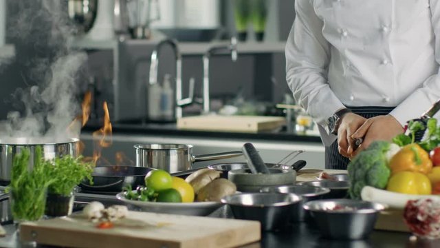 Professional Chef Fires up Oil on a Pan. Flambe Style Cooking. He Works in a Modern Kitchen with Lots of Ingredients Lying Around.  Shot on RED EPIC-W 8K Helium Cinema Camera.