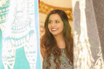 Fototapeta premium Close up of a beautiful smiling young woman hiding behind the andean traditional clothing textile yarn and woven by hand in wool, colorful fabrics background