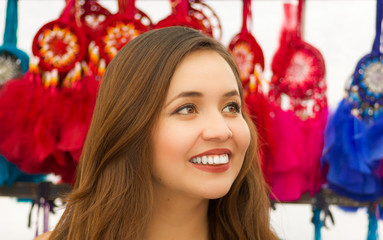 Obraz na płótnie Canvas Close up of a beautiful smiling young woman looking at the horizont in front of blurred colorful catchdreamers, in colorful market background