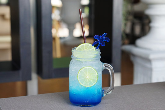 Closeup Glass Of Iced Blue Hawaii Soda With Lemon On Table And On Blurred Background, Summer Cocktail Or Tropical Mocktail.