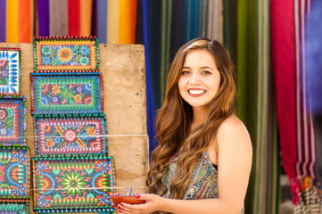 Beautiful smiling young woman holding in her hands a andean traditional bowl with a spoon, colorful fabrics background