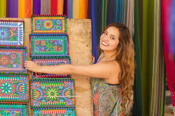 Beautiful smiling young woman touching andean traditional clothing textile yarn and woven by hand in wool, colorful fabrics background