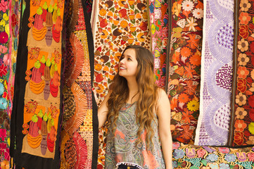 Beautiful smiling young woman touching andean traditional clothing textile yarn and woven by hand in wool, colorful fabrics background