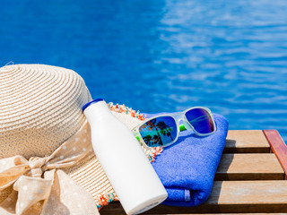 Beach hat, sunglasses, blue towel and sunscreen at the side of swimming pool. Vacation, beach, summer travel concept