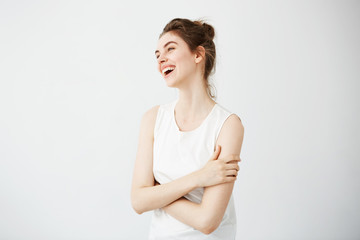 Happy cheerful young girl with bun smiling laughing over white background. Crossed arms.