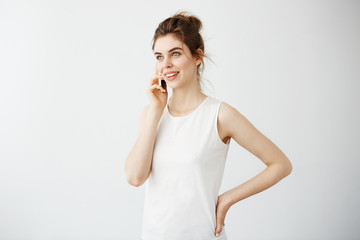 Young beautiful girl with bun smiling speaking on phone over white background.