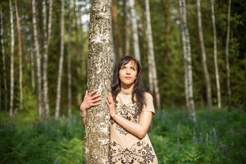 Young girl in a forest park hugging a birch tree and looking at the sun