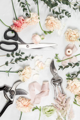 flowers and garden tools. The florist work table with accessories light wooden background.