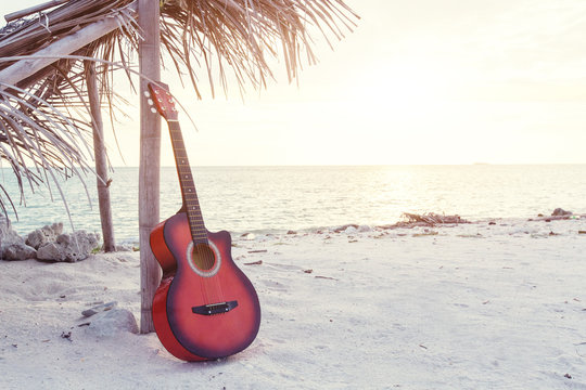 An acoustic guitar standing in the sandy beach under palm tree