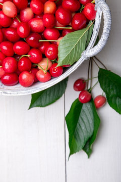 Red cherries in white basket on white wooden background. Cherry close up. Top view.