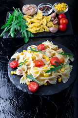 Pasta salad in slate plate with tomatoes cherry, tuna, corn and arugula. Top view. ingredients. Italian food.