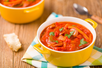 Delicious letcho with fresh vegetables, served in a yellow pot with the fresh bun.