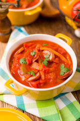 Delicious letcho with fresh vegetables, served in a yellow pot with the fresh bun.