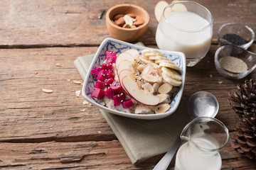 Bowl of oatmeal porridge with bananas, apple, dragon fruit and almonds. Top view
