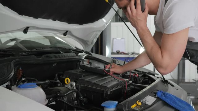 mechanic advises on client's phone, Service station, checks electrical scheme vehicle setup, diagnoses systems and maintains car