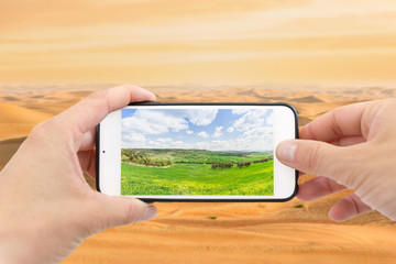 Climate change with desertification process. Smartphone photographing a field, desert in the background.