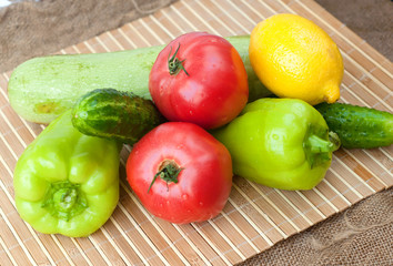 A group of tomatoes, cucumbers, green pepper, zucchini and a lemon on the wooden background