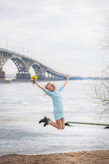 Fototapeta na wymiar A beautiful girl in an amazing blue dress with mimosas on the background of a bridge over the river, she admires, dances, graces and mimosas, jumps from happiness