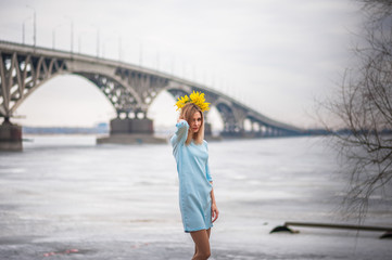 A beautiful girl in an amazing blue dress with mimosas on the background of a bridge over the river, she admires, dances, graces and mimosas, jumps from happiness