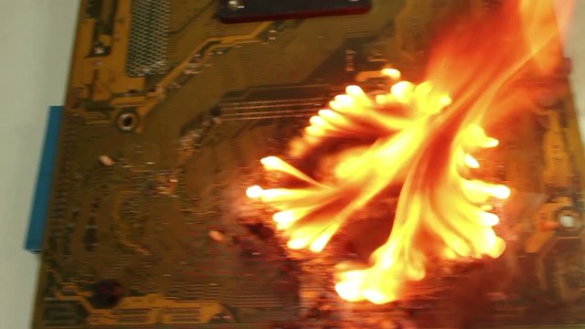 Medium overhead dolly across a big fire on a burning computer motherboard; several passes, then settle . One of a series