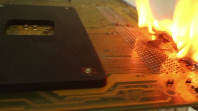 Low angle dolly along burning computer motherboard; the fire finally flickers out. One of a series