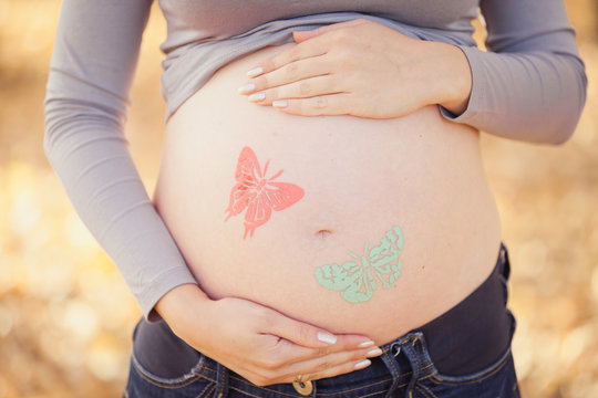 Waiting for baby. Autumn scene of pregnancy, motherhood. Painted butterflies on mum's belly