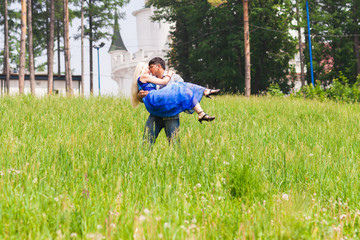 Young man carrying his girlfriend in his arms on grass field. Couple having fun in nature on a summer day.