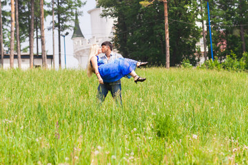 Young man carrying his girlfriend in his arms on grass field. Couple having fun in nature on a summer day.