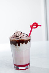 Glass of strawberry milkshake with whipped cocolate cream and fresh strawberries on pink